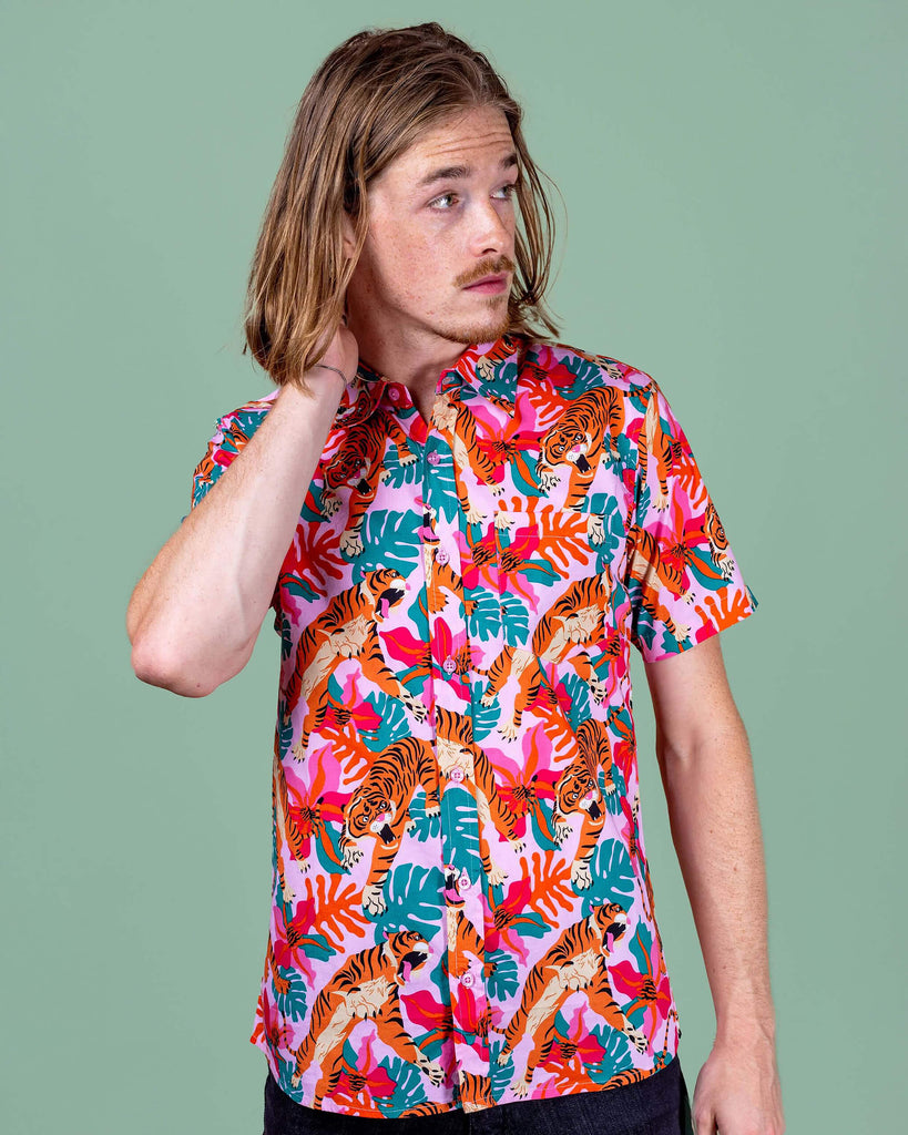 Jack is stood in a photography studio in Hove with a green backdrop wearing Tiger Lily Stretch Short Sleeve Shirt with jeans. The baby pink shirt has an all over print of tigers with flowers and leaves. Jack is posing facing the camera and looking off to one side with one hand on his neck and other down by his side.