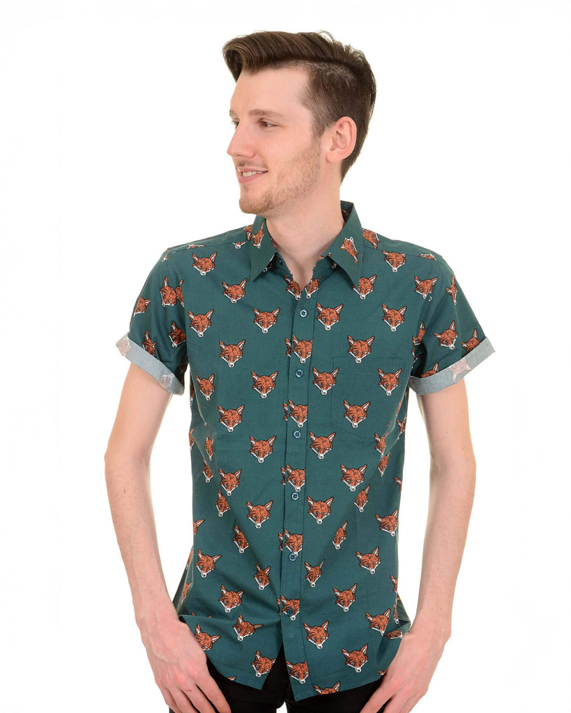 Model is stood in front of a white studio background wearing the preppy foxy short sleeve shirt with black trousers. They are facing the camera posing with both hands resting on the front trouser pockets and looking to the left smiling. Photo is cropped from the knees up.