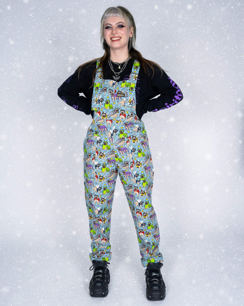 Faeryn modelling Run & Fly ‘Pug Bugs’ dungarees designed by Waffle Mama, standing with hands on hips and smiling. The quirky pug-themed print stands out, paired with a black top and platform boots.