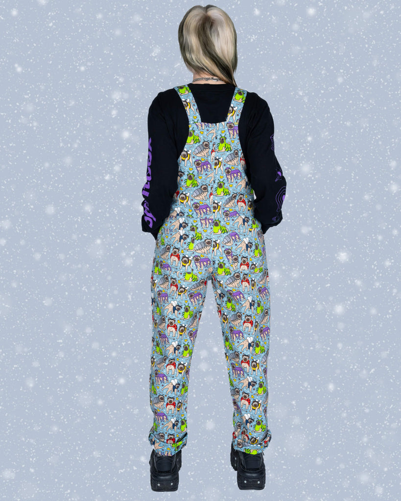 Back view of Faeryn wearing Run & Fly ‘Pug Bugs’ dungarees, highlighting the all-over pug-and-bug print with adjustable dungaree straps and a light blue background.