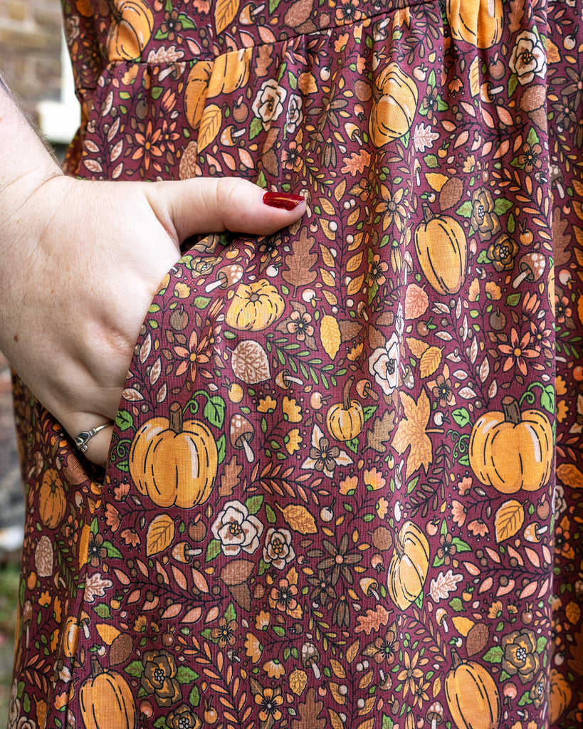 Close-up of Maddie’s hand in the pocket of a rich autumnal pumpkin-themed dress by Run & Fly, designed by Jen James. The fabric showcases an intricate pattern of pumpkins, leaves, and acorns in warm autumnal colours.