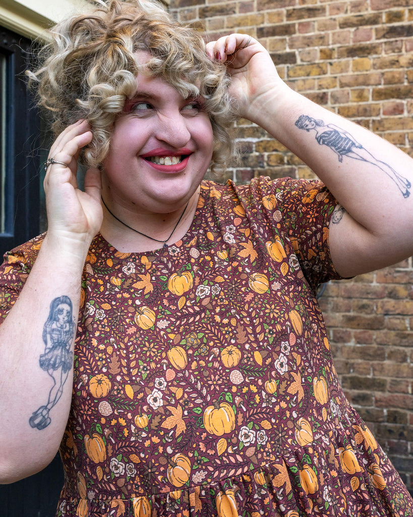 Close-up of Maddie adjusting their curly hair, highlighting the intricate pumpkin print design by Jen James for Run & Fly, filled with tiny details of fall foliage, flowers, and pumpkins.