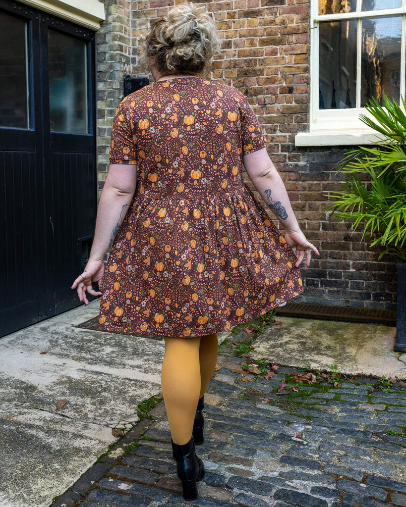 Back view of Maddie in the pumpkin print dress by Run & Fly, showcasing the flowy skirt and intricate design, with mustard tights adding a pop of autumn colour.