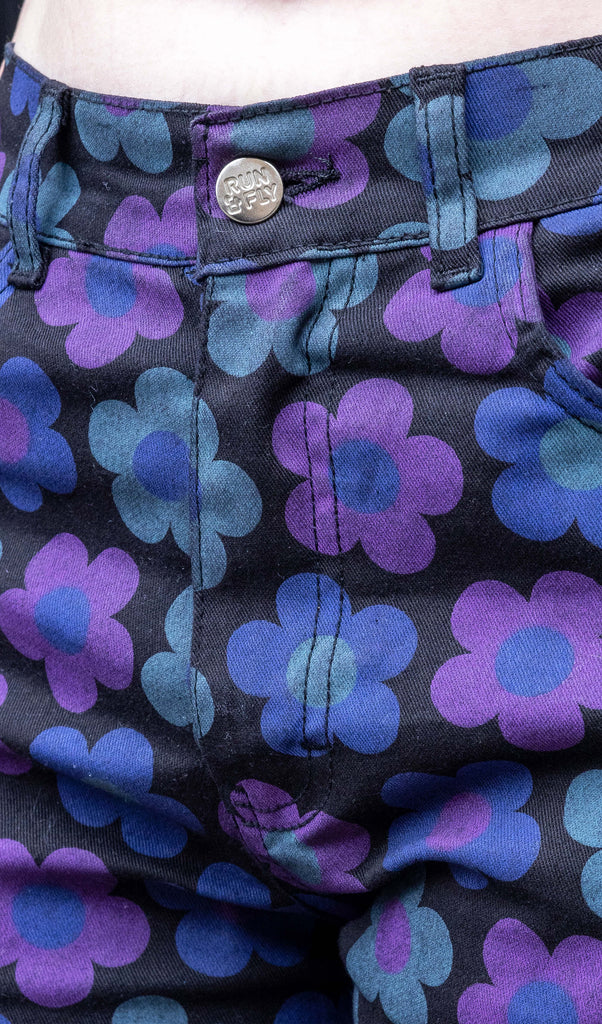 Faeryn a femme non binary person with blue and black hair and dark make up is wearing floral jeans and lilac top in a Hove mews this is a close up of the jeans andRun & Fly Button