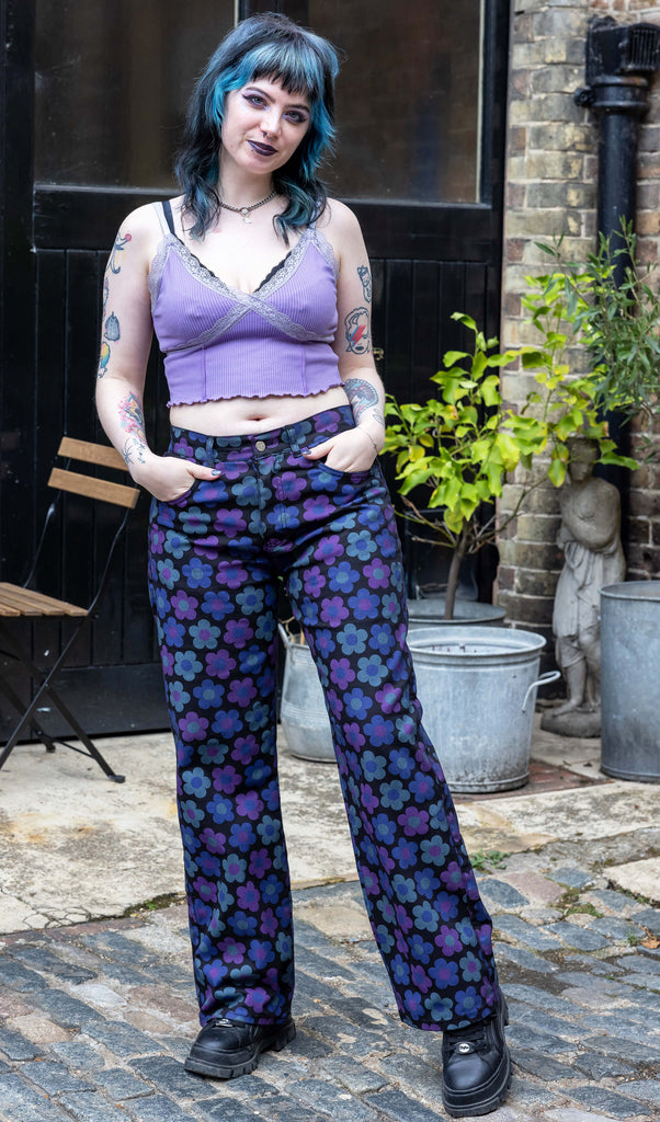 Faeryn a femme non binary person with blue and black hair and dark make up is wearing floral jeans and lilac top in a Hove mews 