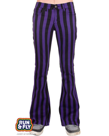 Model is stood in front of a white studio background wearing the purple and black striped bell bottom stretch super flares with grey trainers. They are facing forward and photo is cropped from the waist down.