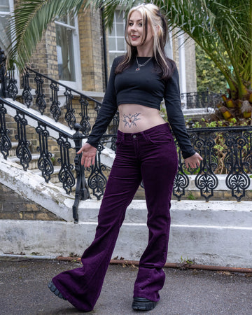 Model poses in the Run & Fly Midnight Purple Corduroy Flares paired with a long-sleeve black crop top, showing off the high-waisted fit and dramatic bell bottoms.