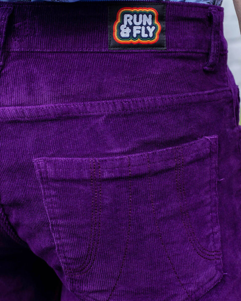 Close up of the back waistband run and fly label on the purple corduroy bell bottom flares, paired with the blue safari shirt. Photo is cropped in on the back waistband.