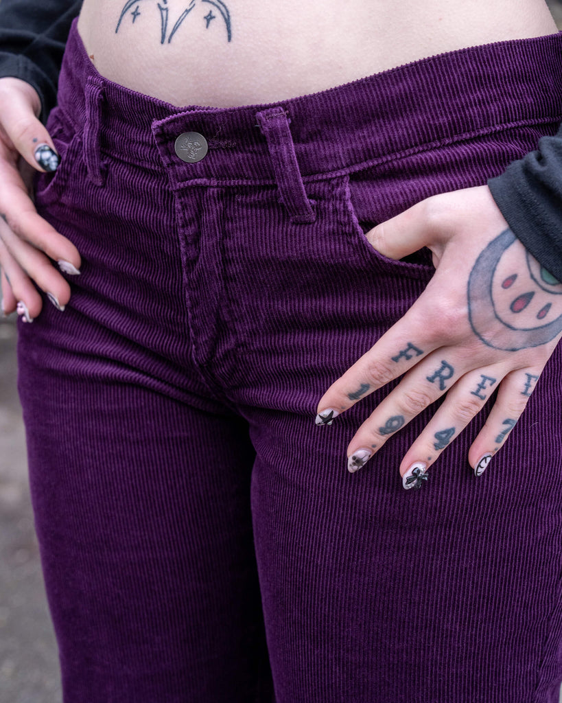 Close-up of the front waistband and pockets of the Run & Fly Midnight Purple Corduroy Bell Bottom Flares, showing rich purple fabric, silver button, and vertical cord texture.