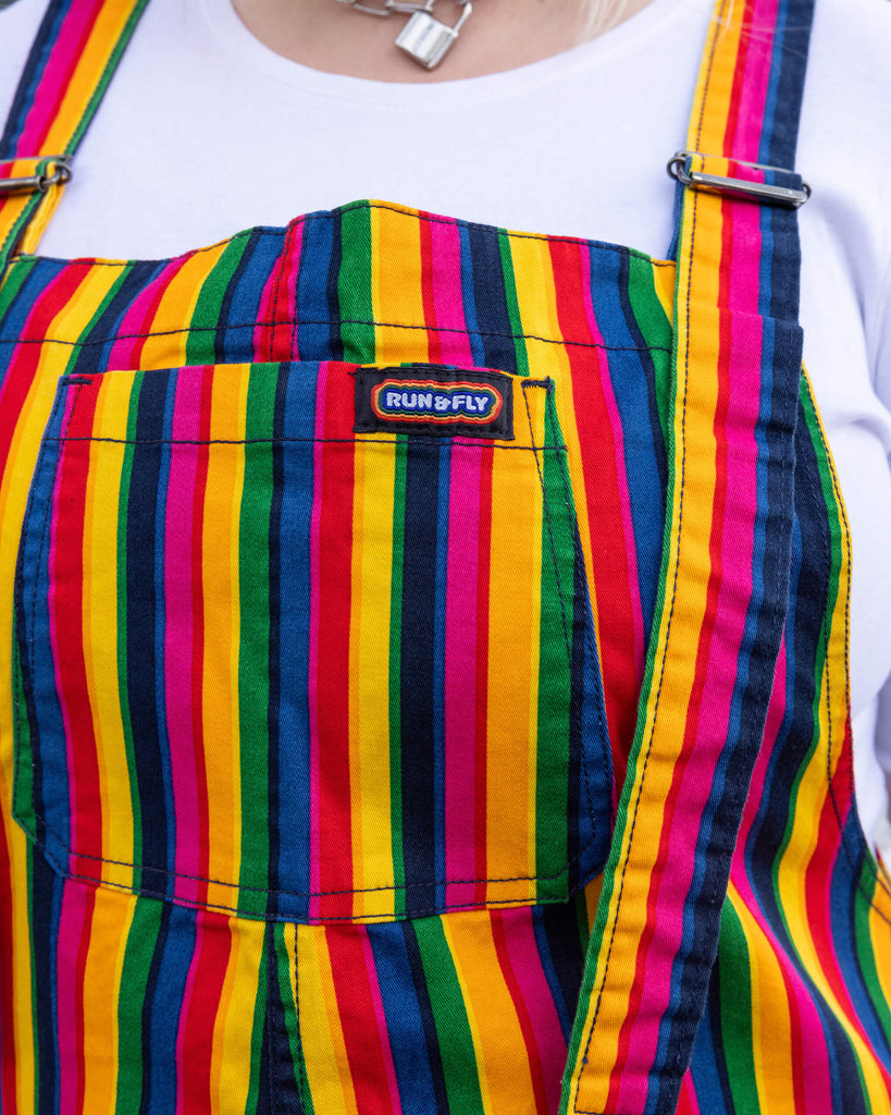 Close-up of Run & Fly’s rainbow-striped dungarees pocket. The design features vertical stripes in vibrant colours, with a small Run & Fly logo on the chest pocket. Known for their ethical production, Run & Fly’s dungarees combine bold style with slow fashion principles.