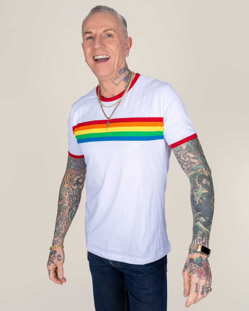 James laughing in the white rainbow stripe T-shirt. The crisp white fabric contrasts with vibrant rainbow colours, complemented by his detailed arm tattoos.