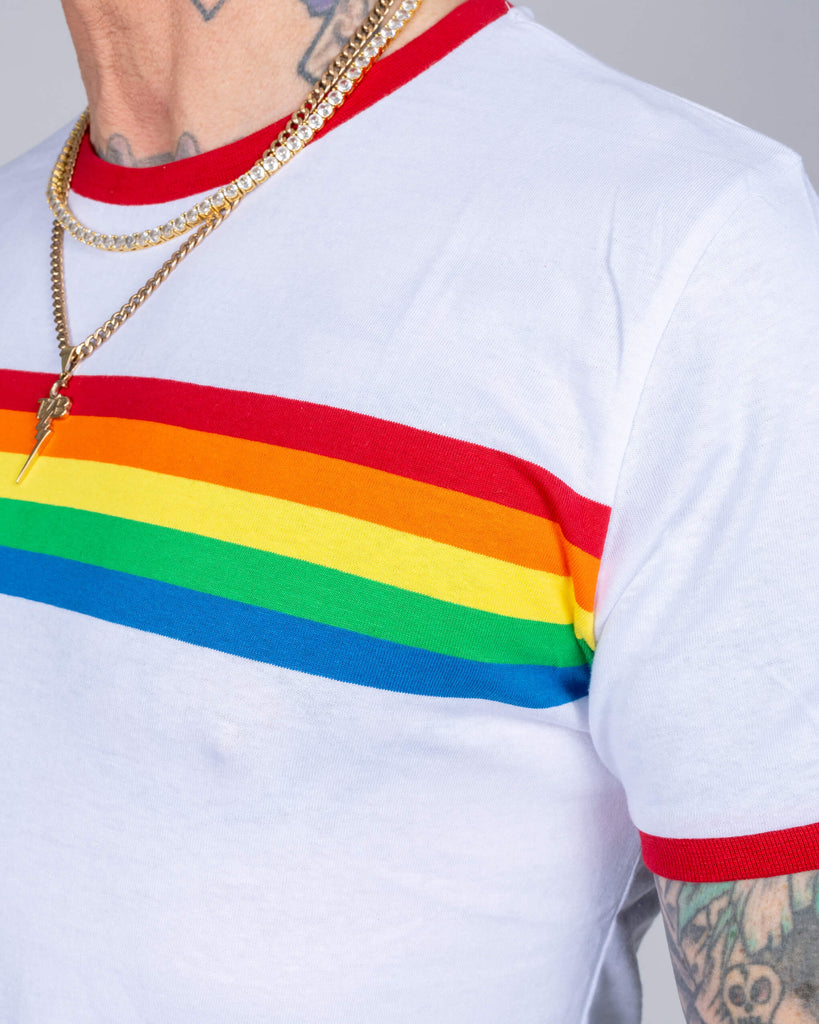 Close-up of James wearing the white T-shirt, showing the rainbow stripe’s vivid colours and the red trimmed neckline, paired with gold chains for added flair.