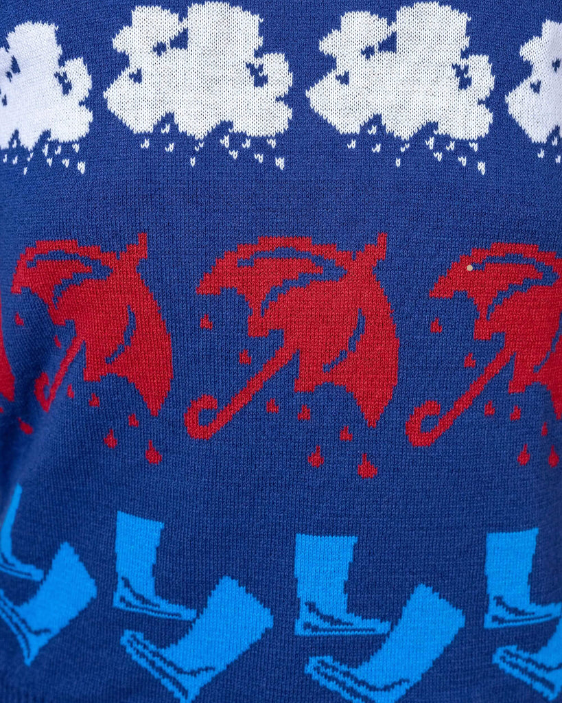 Close of the made in england run and fly rainy days acrylic jumper. The jumper is a blue base with a red, orange, white and blue stripe section, a stripe of rain clouds, a stripe of red umbrellas and a stripe of light blue welly boots. The back and sleeves are a plain blue.