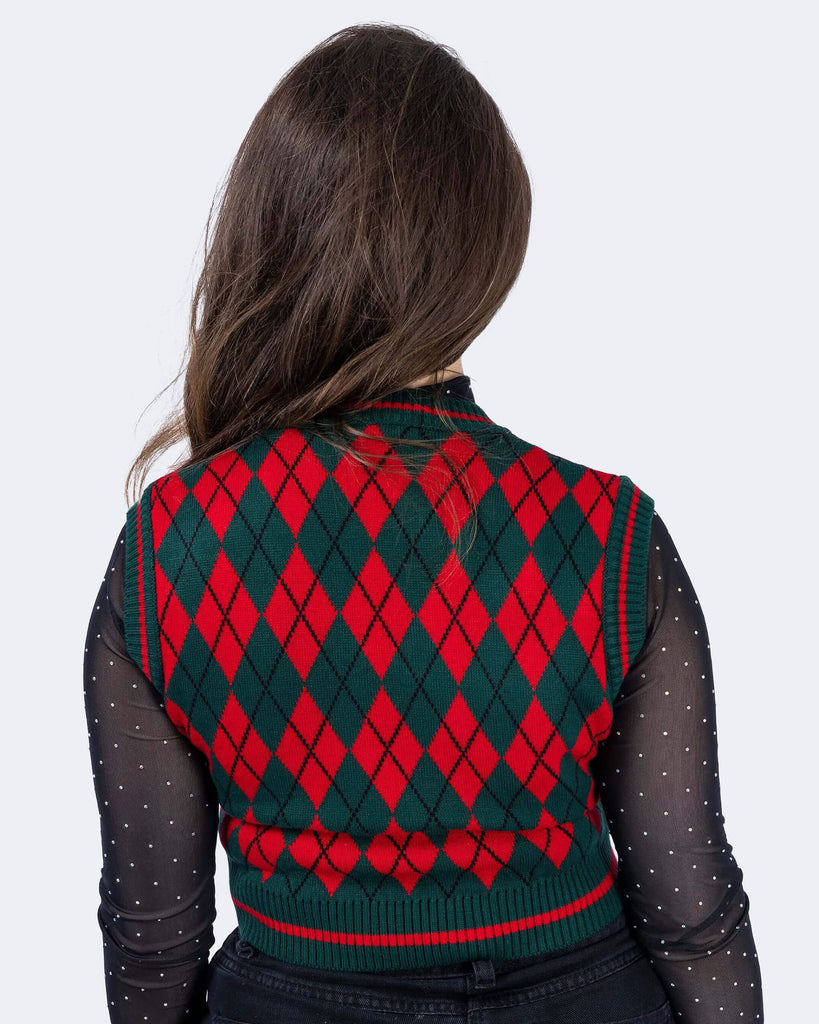 Charlotte is wearing Red and Green Argyle Knitted Tank Top with a long sleeve black mesh top underneath with white polka dots and black trousers. Charlotte is stood in front of a white background with her back to the camera and the photo is cropped from the thighs down.