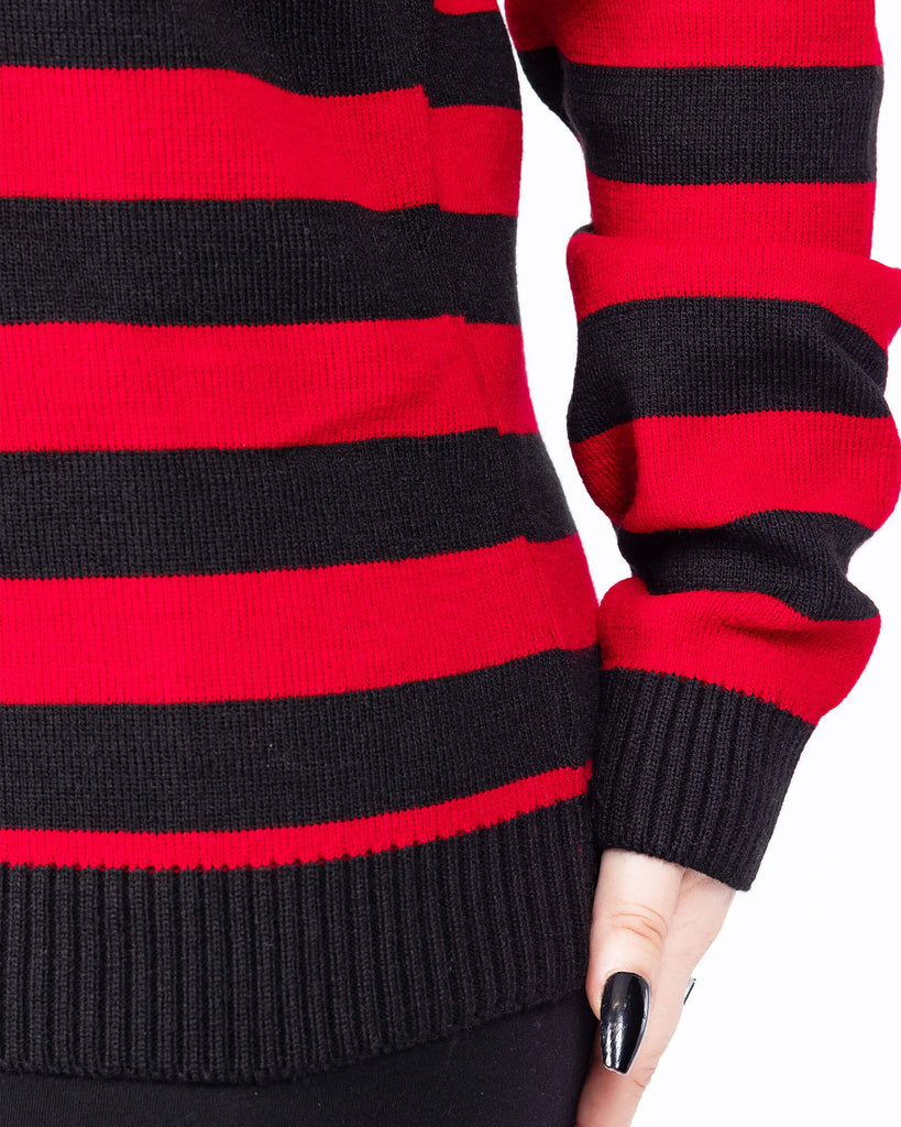 Close up of the Red and Black Striped Jumper worn by a femme model with short blonde hair with black trousers. She is facing forward to highlight the black hem and sleeve trim with alternating black and red stripes all over.