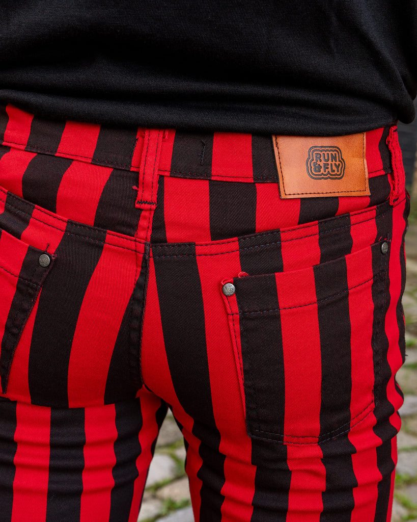 Close-up of the back of Run & Fly’s red and black striped skinny jeans, highlighting the brown leather logo patch on the waistband. The bold vertical stripes and detailed stitching showcase the brand’s commitment to quality slow fashion.