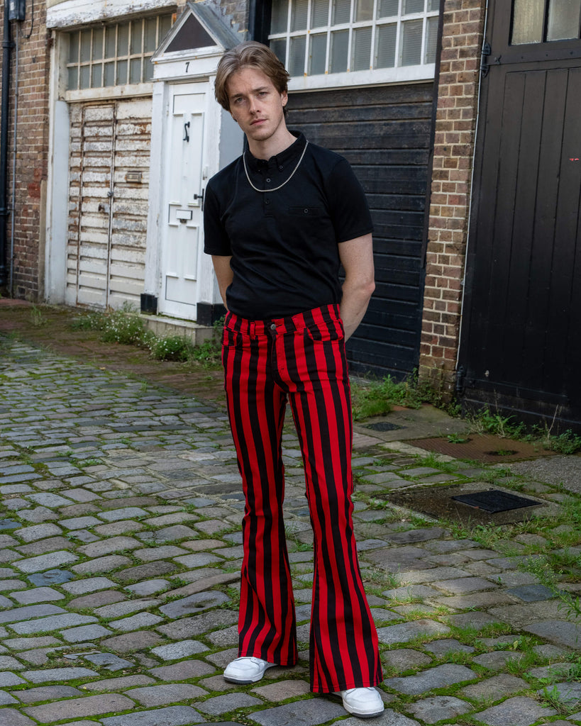 Jack is stood outside in Hove in a mews wearing Red & Black Striped Bell Bottom Stretch Super Flares with a black tshirt tucked in and white trainers. He is posing toward the camera with one leg in front of the other and hands behind his back