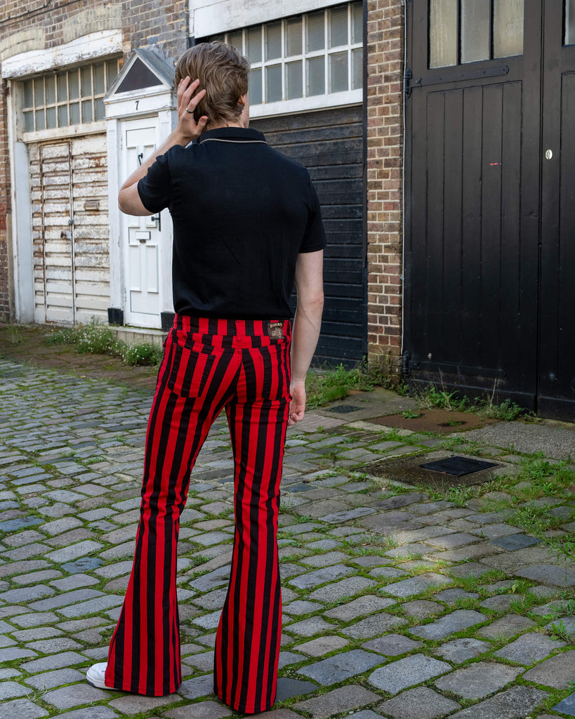 Jack is stood outside in Hove in a mews wearing Red & Black Striped Bell Bottom Stretch Super Flares with a black tshirt tucked in and white trainers. He is stood with his back to the camera and has one hand on his head and the other resting by his side.