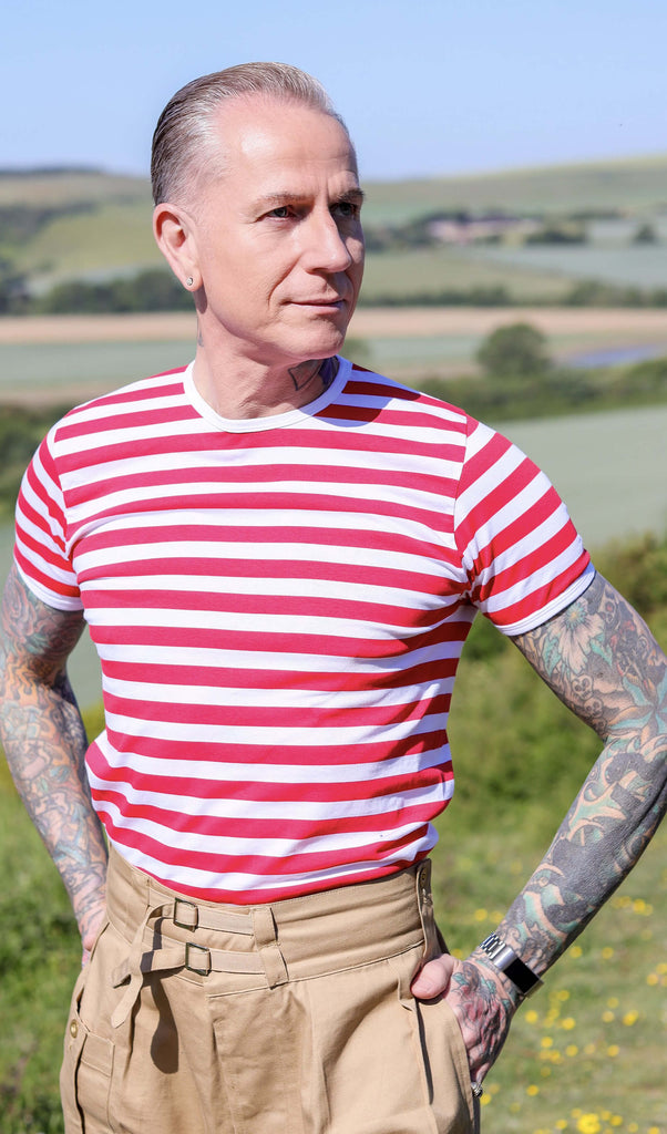 Jim is stood outside in a field wearing the white and red stripe short sleeve tshirt with beige cargos. They are facing forward posing with both hands in their front trouser pockets whilst looking off to the right. Photo is cropped from the hips up.