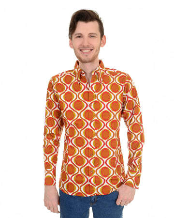 Model is stood in front of a white studio background wearing the retro mod geometric psychedelic printed 70s shirt with blue jeans. They are facing forward with both arms resting by their side whilst smiling. Photo is cropped from the hips up.