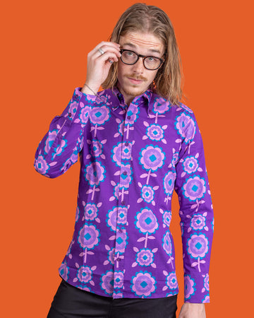 Jack, a male model with shoulder length hair and glasses is stood in front of an orange backdrop at a photography studio in Hove wearing Purple Retro Flowers Long Sleeve Shirt with black trousers. Jack is facing the camera posing with his hand on his glasses and other down by his side. The photo is cropped at the knees.