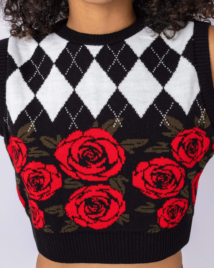 Cindy is stood in front of a white backdrop at a photography studio in Hove wearing the Rose and Argyle Knitted Tank Top. The black tank top has a black and white argyle print on the top half with a red rose pattern on the bottom half of the tank top. Cindy is facing the camera with her hands on her hips. 