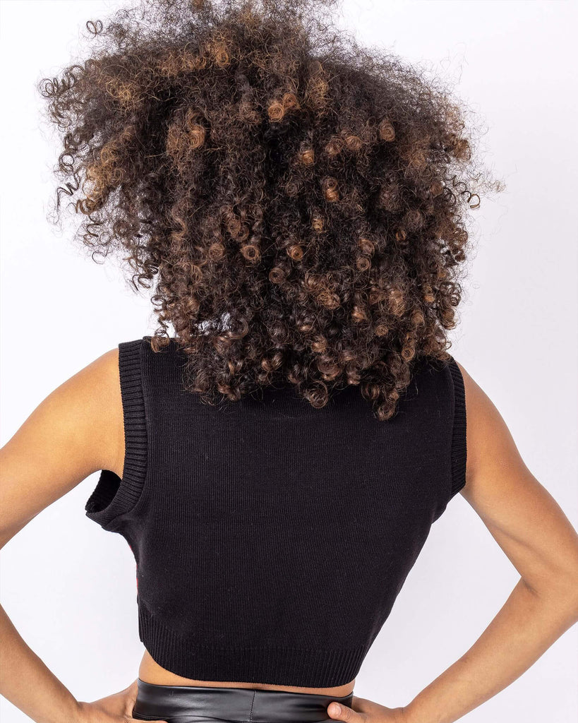 Cindy is stood in front of a white backdrop at a photography studio in Hove wearing the Rose and Argyle Knitted Tank Top. The black tank top has a black and white argyle print on the top half with a red rose pattern on the bottom half of the tank top. Cindy is stood with back to the camera and hands on her hips to show the plain back of the tank top. 