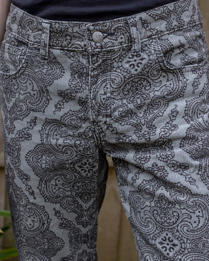 Close-up of Run & Fly’s Silver Hendrix flares on model Jack, highlighting the intricate black paisley pattern against the silver fabric. The texture and details of the corduroy fabric are visible.