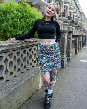 A person smiles while wearing the Run & Fly Boho Summer A-Line Skirt paired with a black crop top and chunky boots, showing tattoos and standing by a decorative stone wall in a city street.