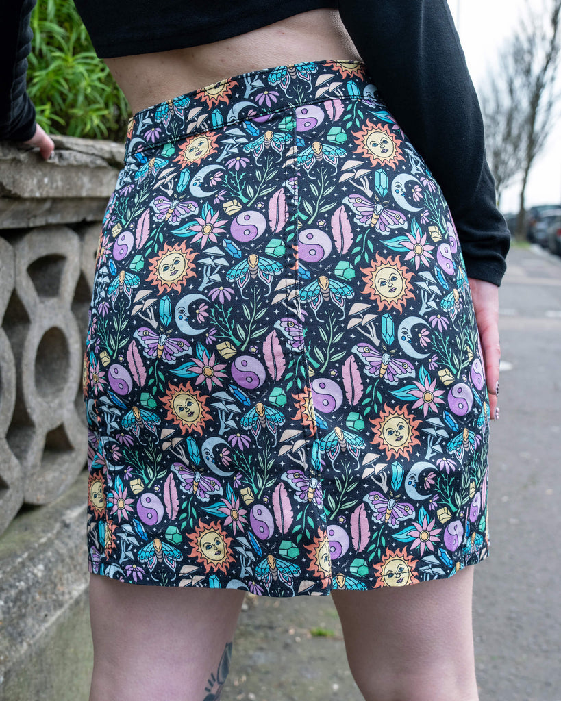 Close-up of the back of the Run & Fly Boho Summer A-Line Skirt showing a colourful print of suns, moons, flowers, crystals, butterflies and yin-yangs on black stretch cotton.