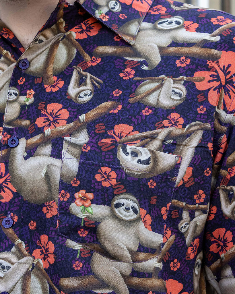 Declan a male in his 20's with a beard and glasses is wearing a sloth shirt with Hawaiian flowers on and beige cargo trousers on a street in Hove this is a close up of the shirts pocket