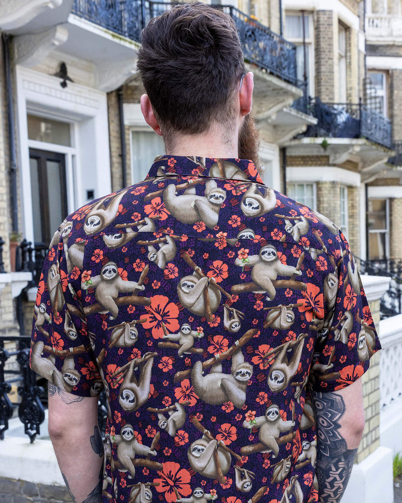 Declan a male in his 20's with a beard and glasses is wearing a sloth shirt with Hawaiian flowers on and beige cargo trousers on a street in Hove he is facing the back.