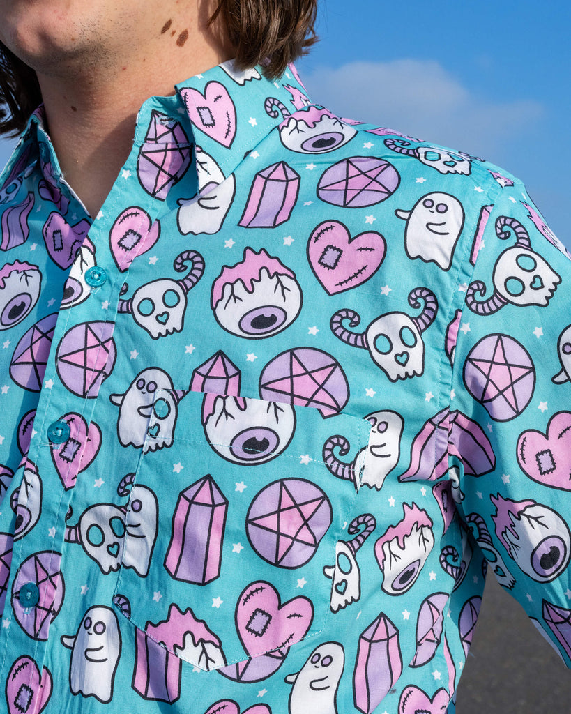 Close-up of Run & Fly's Spooky Stuff shirt, showcasing whimsical ghostly motifs with skulls, candy canes, and pentagrams in pastel shades on teal. A playful and ethical choice for slow fashion enthusiasts.