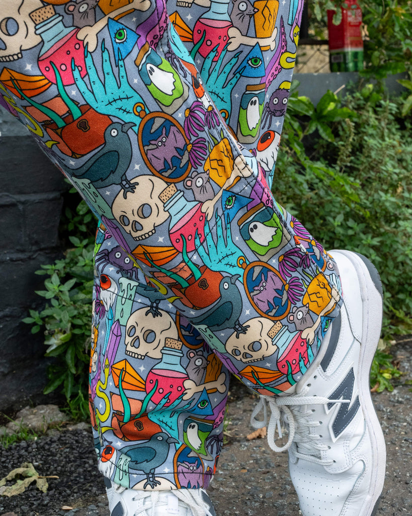 Close up of the legs of the Run & Fly Halloween: Spooky Stuff Stretch Twill Dungarees. The light blue dungarees have an all over print of various Halloween themed items such as skulls, snakes, eyeballs, ghosts, bats, crows, candles, potions, crystals and more. Close up shows the matching turn-ups on the dungarees