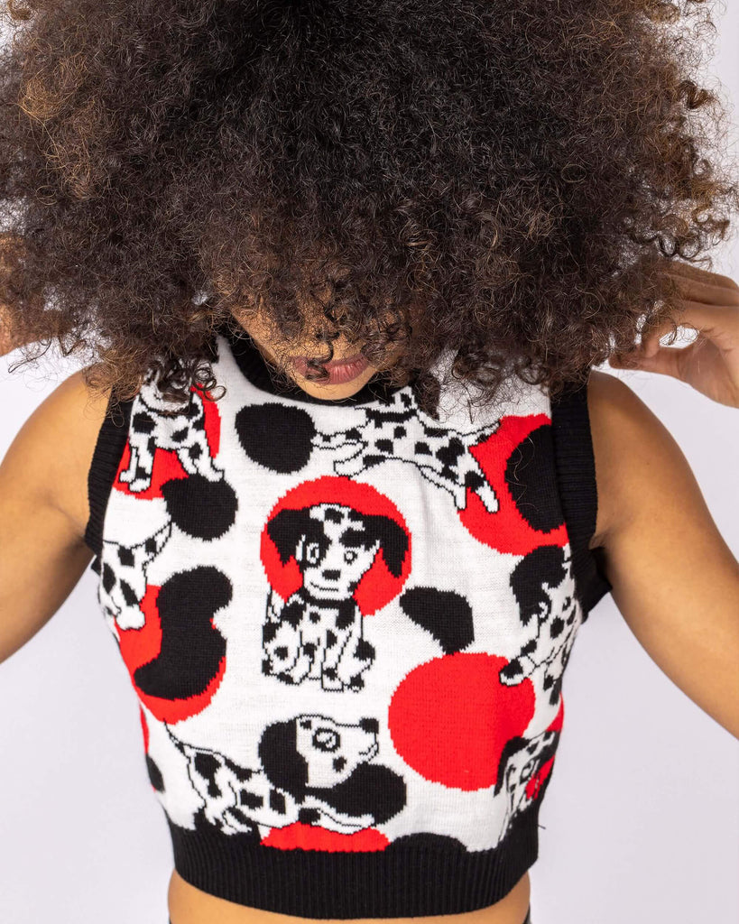 Cindy is stood in front of a white studio background wearing the seeing spots Dalmatian knitted tank top with leather look leggings. They are facing forward with both hands behind their head whilst looking down. Photo is cropped from the hips up.