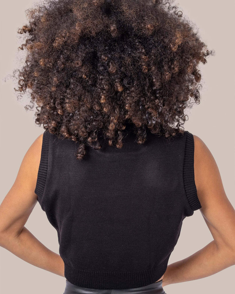 Cindy is stood in front of a white studio background wearing the seeing spots Dalmatian knitted tank top with leather look leggings. They are facing away from the camera posing with both hands on their hips. Photo is cropped from the hips up.