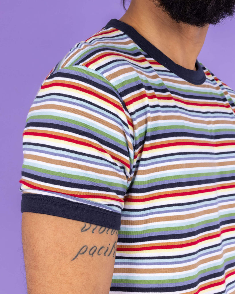 Close up of Richard wearing the Retro Multi Striped Ringer Tee.  The short sleeved t shirt has horizontal stripes going across it in navy blue, white, orange, brown, yellow, pastel blue and green.
