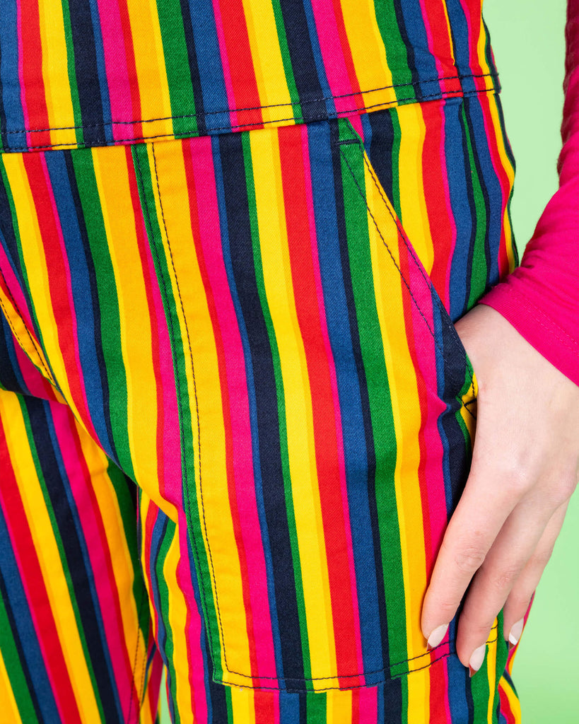 Close-up of the rainbow stripe dungarees by Run & Fly, showing the vertical stripes in red, blue, green, yellow, and pink. The bright pattern adds a fun, playful feel to the look. Run & Fly is a small, ethical, slow fashion company.