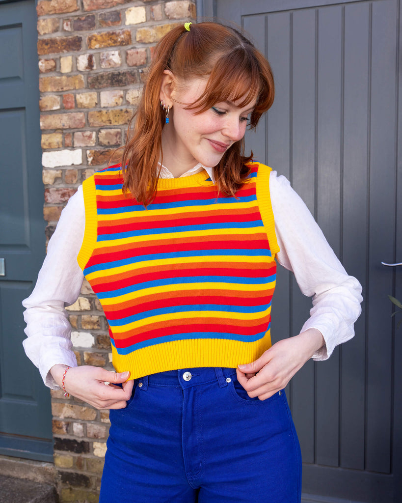 Tasha is a smiley female red haired model with a fringe wearing a white shirt and cobalt jeans with a striped yellow, blue, orange and red tank top. She is stood in a mews in Hove