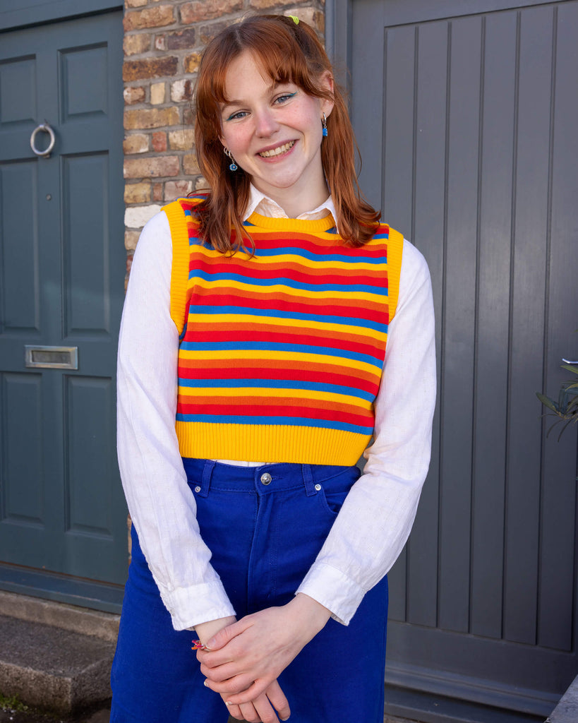 Tasha is a smiley female red haired model with a fringe wearing a white shirt and cobalt jeans with a striped yellow, blue, orange and red tank top. She is stood in a mews in Hove