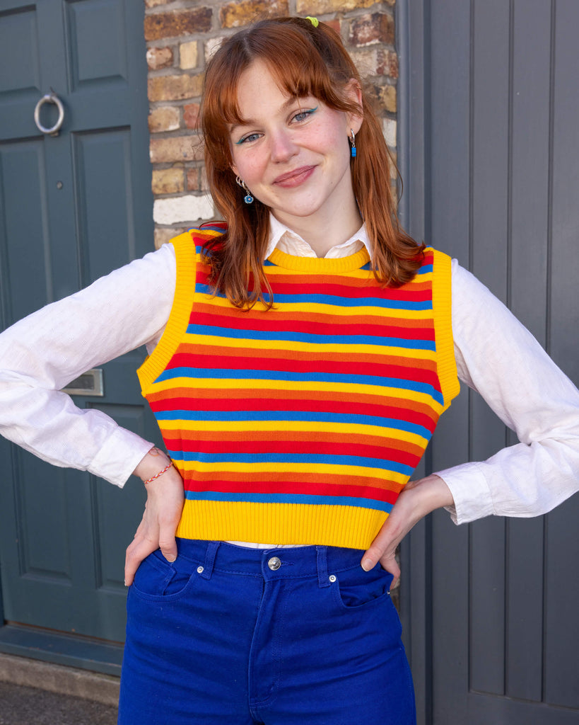 Tasha is a smiley female red haired model with a fringe wearing a white shirt and cobalt jeans with a striped yellow, blue, orange and red tank top. She is stood in a mews in Hove with her hands on her hips