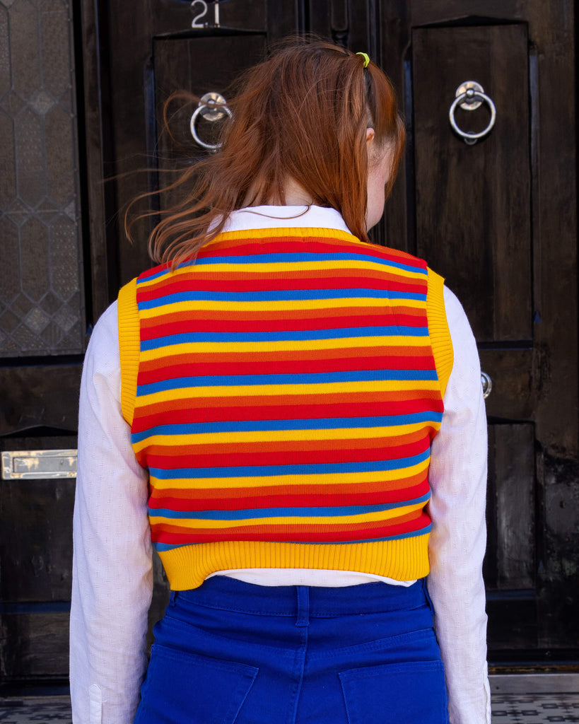 Tasha is wearing a white shirt and cobalt jeans with a striped yellow, blue, orange and red tank top. She is stood in a mews in Hove with her back to the camera to show the back of the tank top