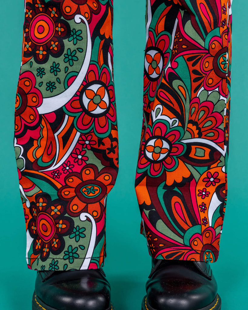 Amy a blonde model with bobbed hair is wearing a white long sleeved cropped tee with jazzy 70's swirly flares with black boots on a green background 