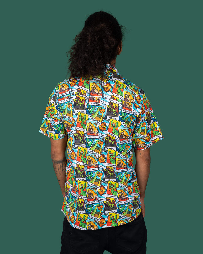 Back view of a person wearing a Run & Fly short-sleeve shirt with a vibrant dinosaur tarot card pattern. The shirt showcases colourful dinosaur illustrations on tarot cards, embodying the brand's unique and ethical fashion principles.