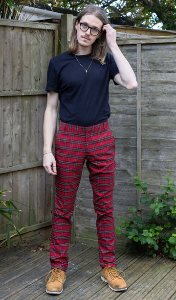 Jack is stood in a garden wearing the retro mod stretch red royal Stewart tartan trousers with a short sleeve black shirt and white trainers.