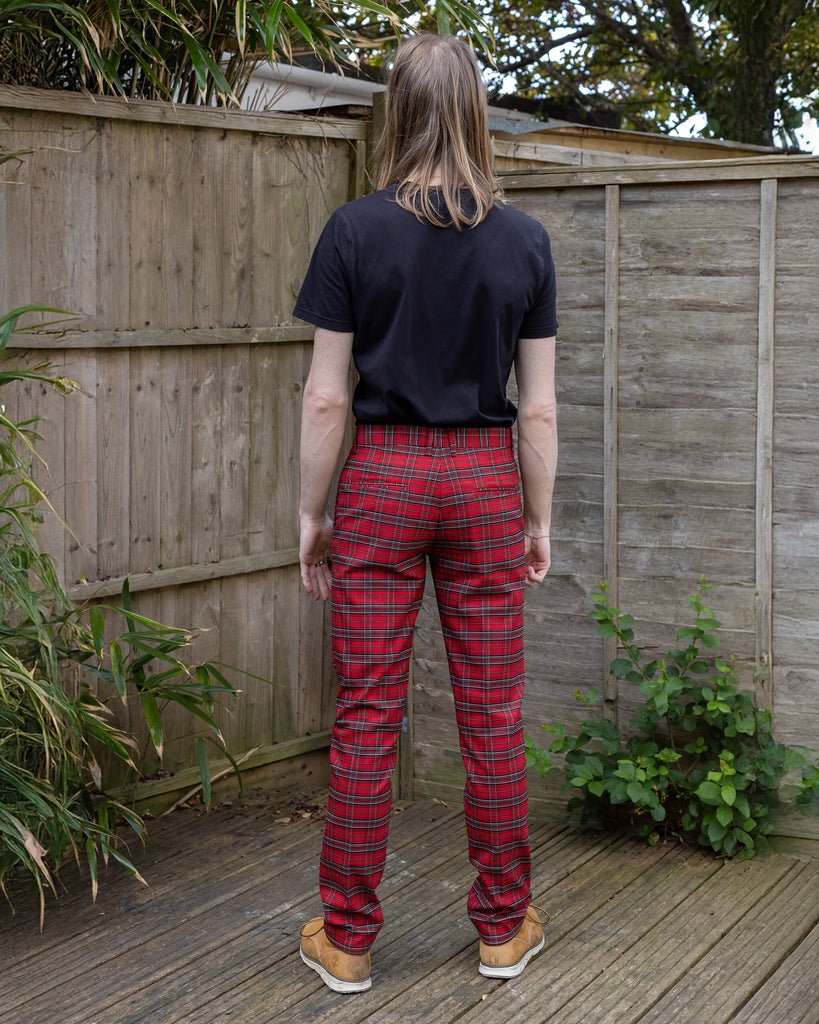 Jack is stood in a garden wearing the retro mod stretch red royal Stewart tartan trousers with a short sleeve black shirt and white trainers.