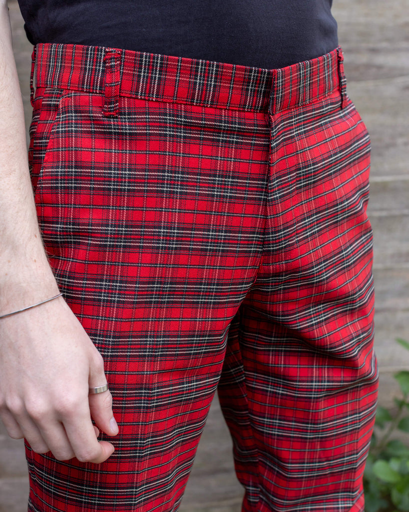 Jack is stood in a garden wearing the retro mod stretch red royal Stewart tartan trousers with a short sleeve black shirt and white trainers.