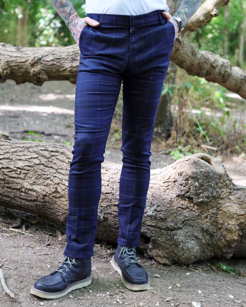 Jim is stood in a forest area wearing the retro mod stretch navy plaid tartan slim skinny fitting trousers with a white short sleeve tshirt and brown boat shoes. They are facing forward with both hands in the side trouser pockets. Photo is cropped from the waist down.