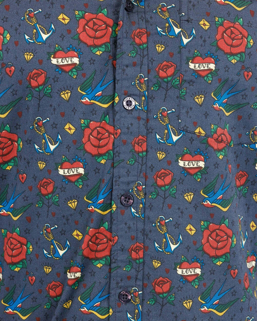 Close up of Retro Old School Tattoo Print Short Sleeve Shirt. The print has traditional tattoo style red roses, blue swallows, yellow envelopes, anchors and valentines love heart.