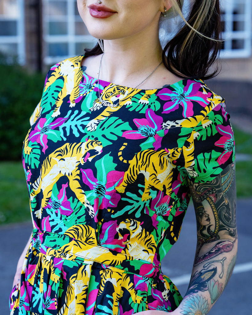 Close-up of Run & Fly tiger print tea dress showing detail of pink tropical flowers, green monstera leaves and bold yellow tigers on black fabric. Ethically made slow fashion from the UK.